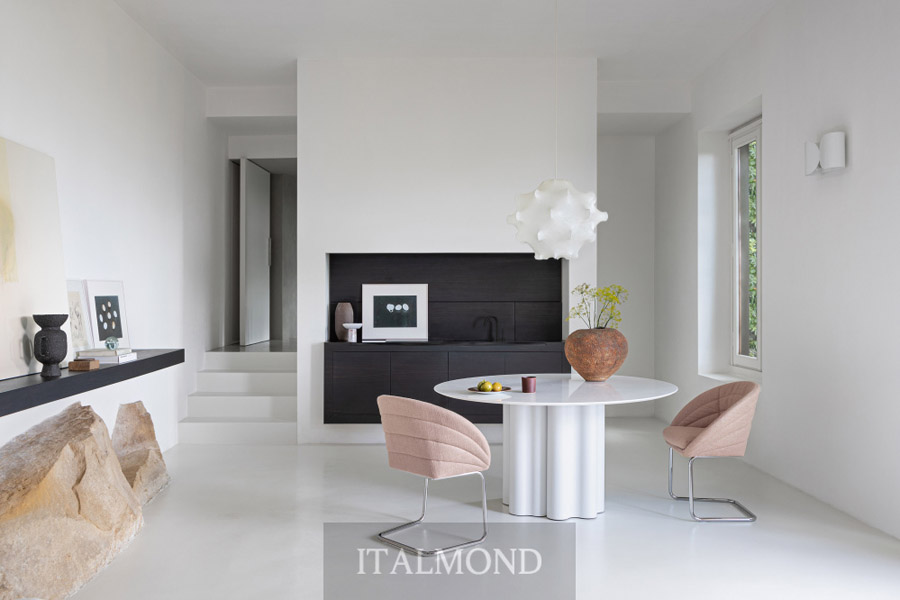 Белая столовая зона с круглым столом, розовыми стульями и камином